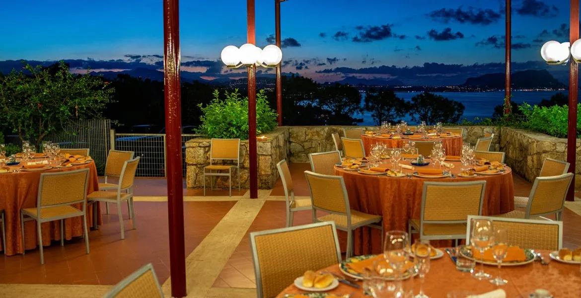 Terrazza ristorante all'aperto con tavoli rotondi apparecchiati e vista sul mare al tramonto