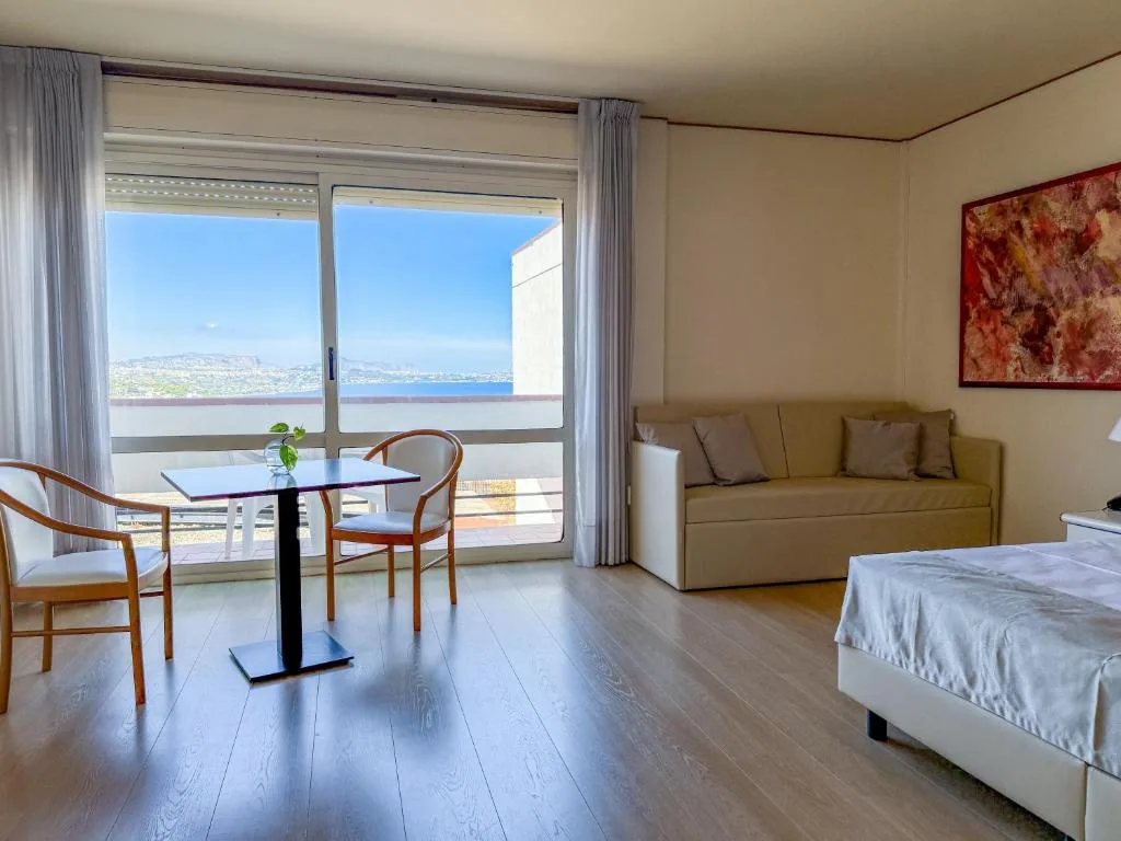 Soggiorno di camera con divano, tavolino e ampia vetrata con vista sul mare
