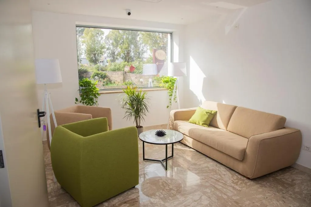 Salottino luminoso con divano beige, poltrona verde e ampia finestra sul verde