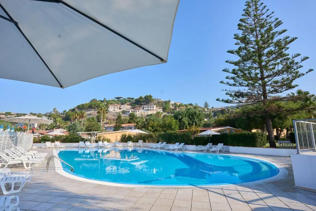 Piscina vista da sotto un ombrellone con pino marittimo e colline sullo sfondo