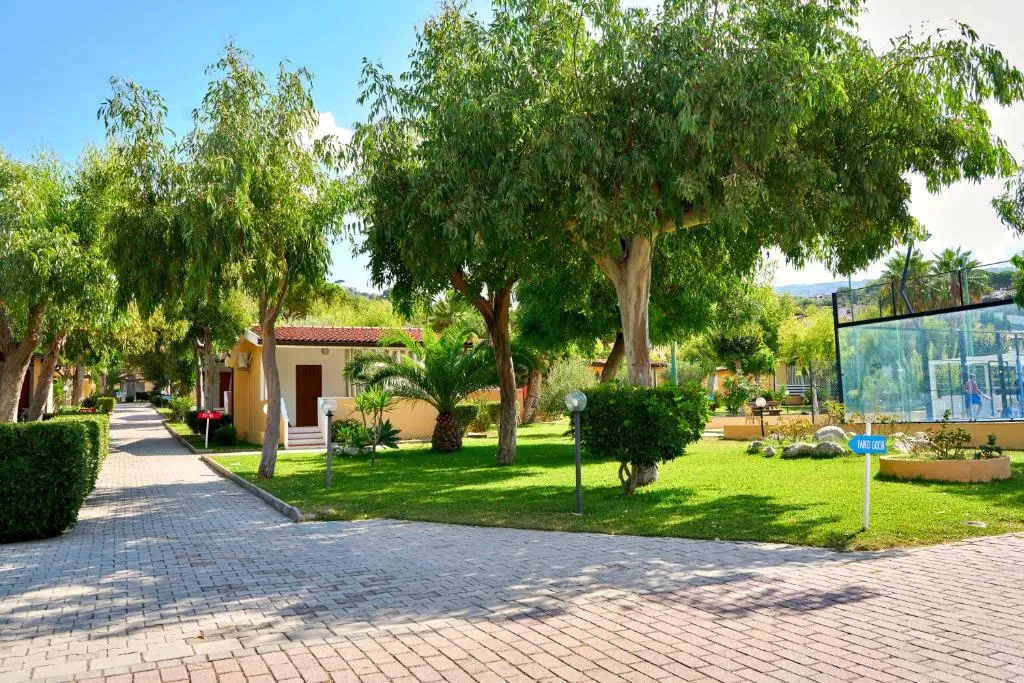 Vialetto pedonale del villaggio tra alberi, bungalow e prato verde