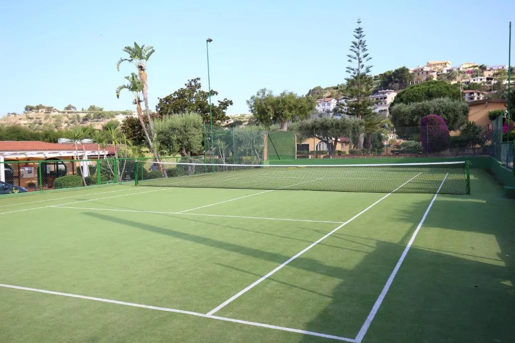 Campo da tennis in erba sintetica circondato da palme e colline