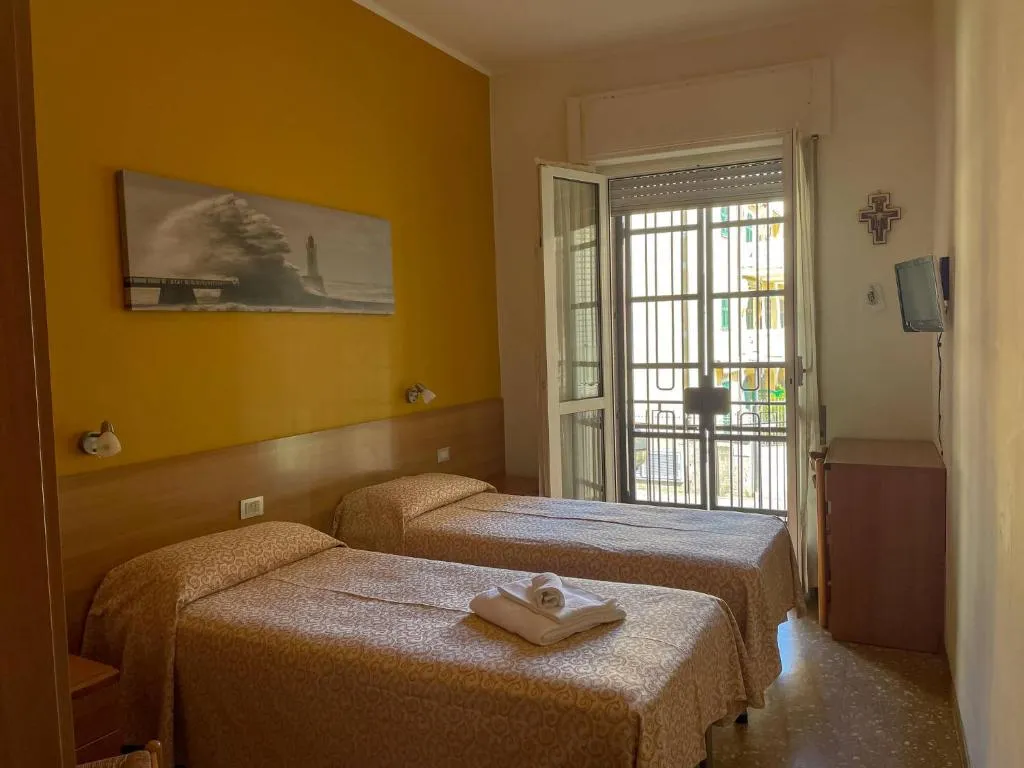 Camera con due letti singoli, parete gialla e balcone con porta finestra