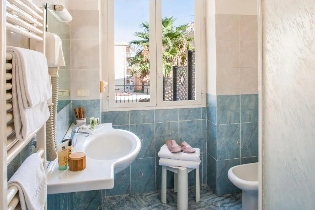 Bagno con piastrelle verdi, lavabo, finestra con vista sulle palme