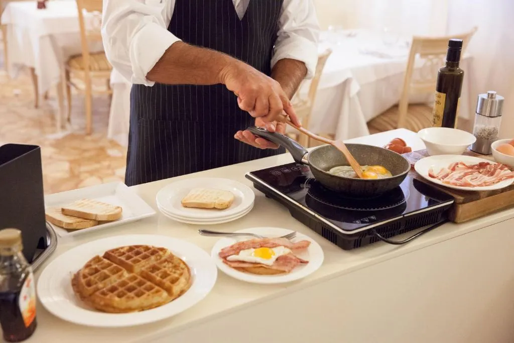 Chef cucina uova e bacon con piastra a induzione durante la colazione
