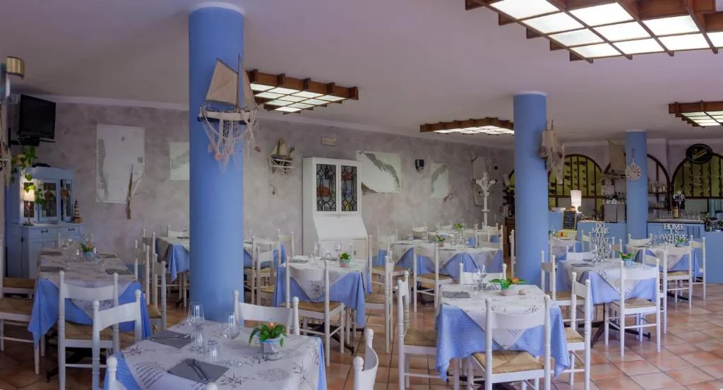 Sala ristorante interna in stile marinaro con colonne azzurre, tavoli con tovaglie bianche e blu