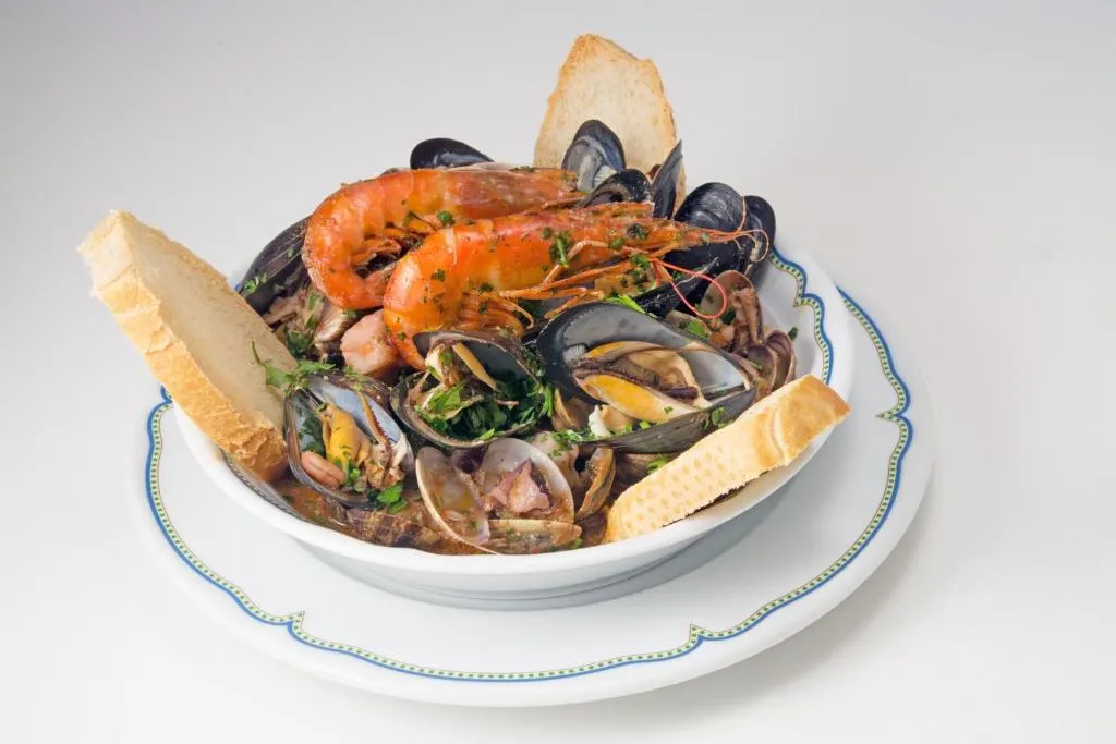 Piatto di zuppa di pesce con cozze, vongole e gamberi accompagnata da pane