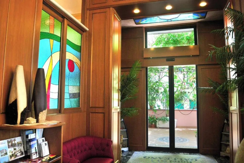 Hall dell'hotel con vetrate decorate, rivestimenti in legno e divanetto bordeaux