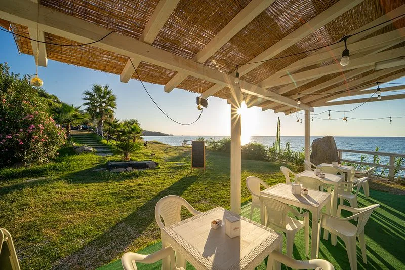 Area ristoro con pergolato in canne e tavoli affacciati sul mare al tramonto