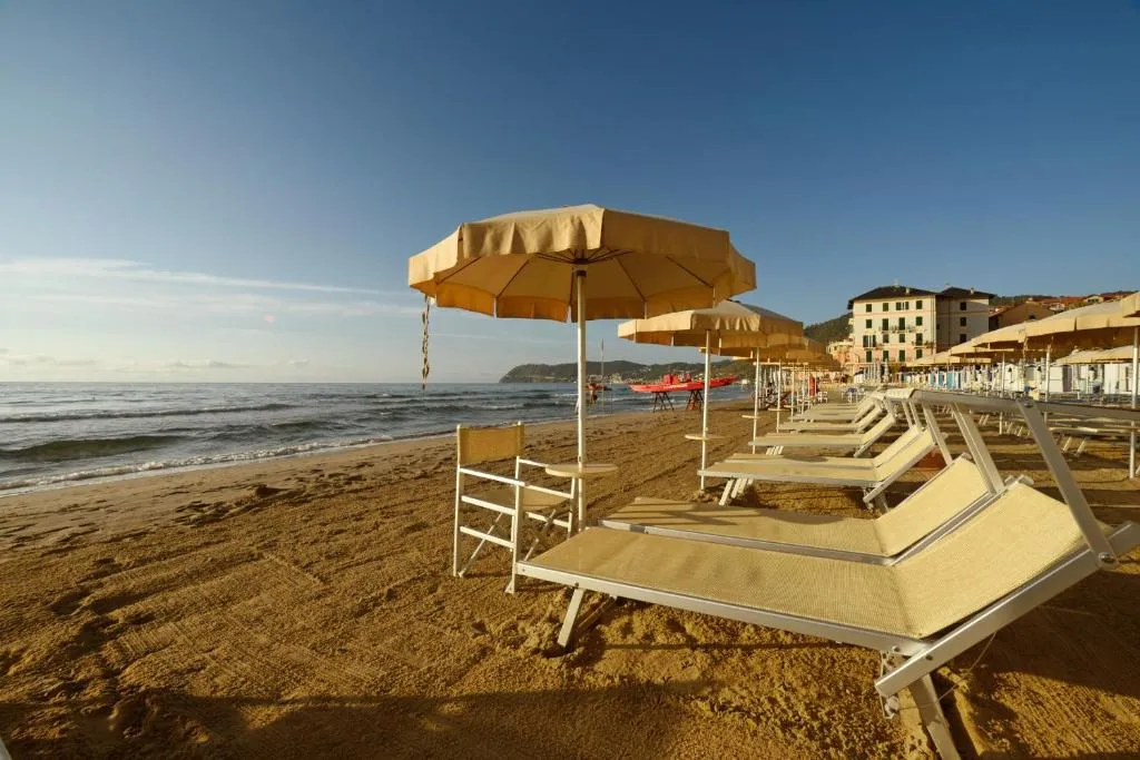 Spiaggia sabbiosa con lettini e ombrelloni beige al tramonto e vista sul mare