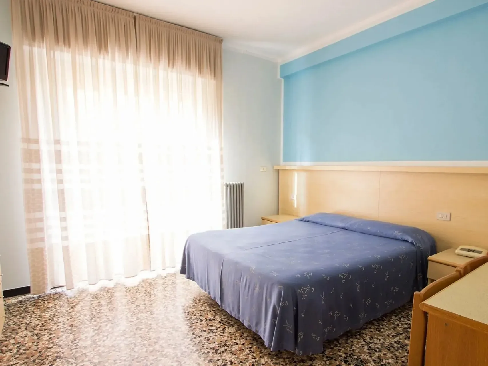 Camera luminosa con letto matrimoniale, parete azzurra e ampia finestra