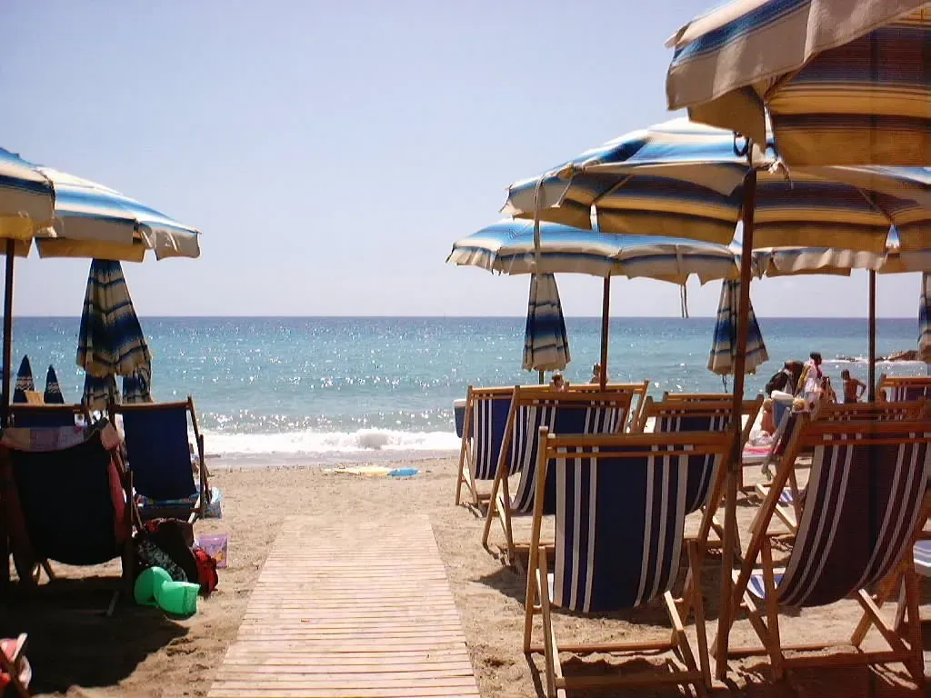 Spiaggia con ombrelloni a righe, lettini in legno e vista sul mare