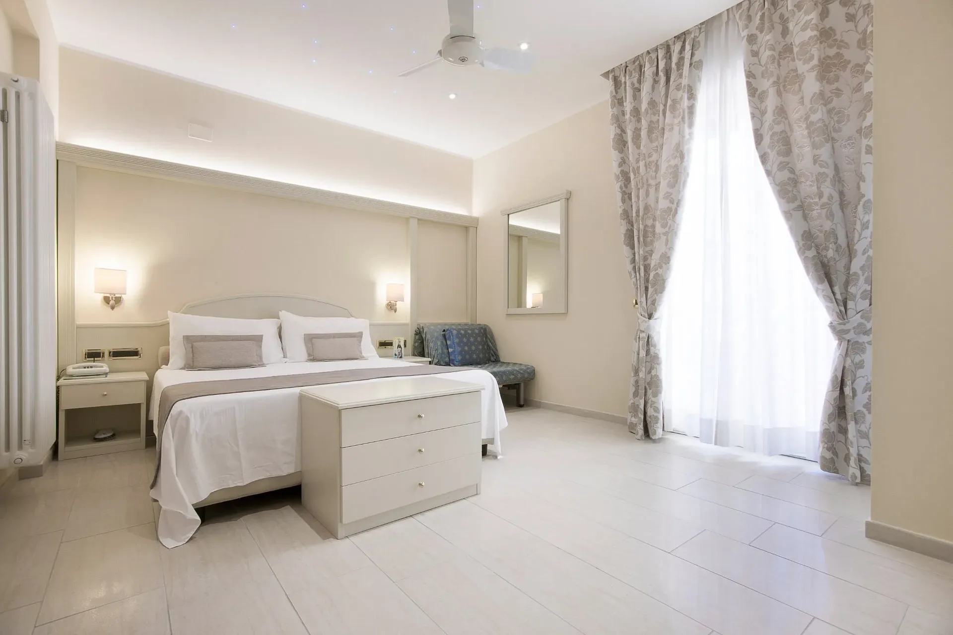 Camera elegante con letto matrimoniale, cassettiera e tende floreali