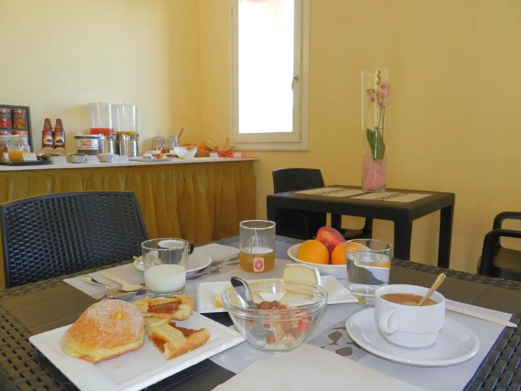 Tavolo della colazione apparecchiato con cornetti, frutta, latte e caffè con buffet sullo sfondo