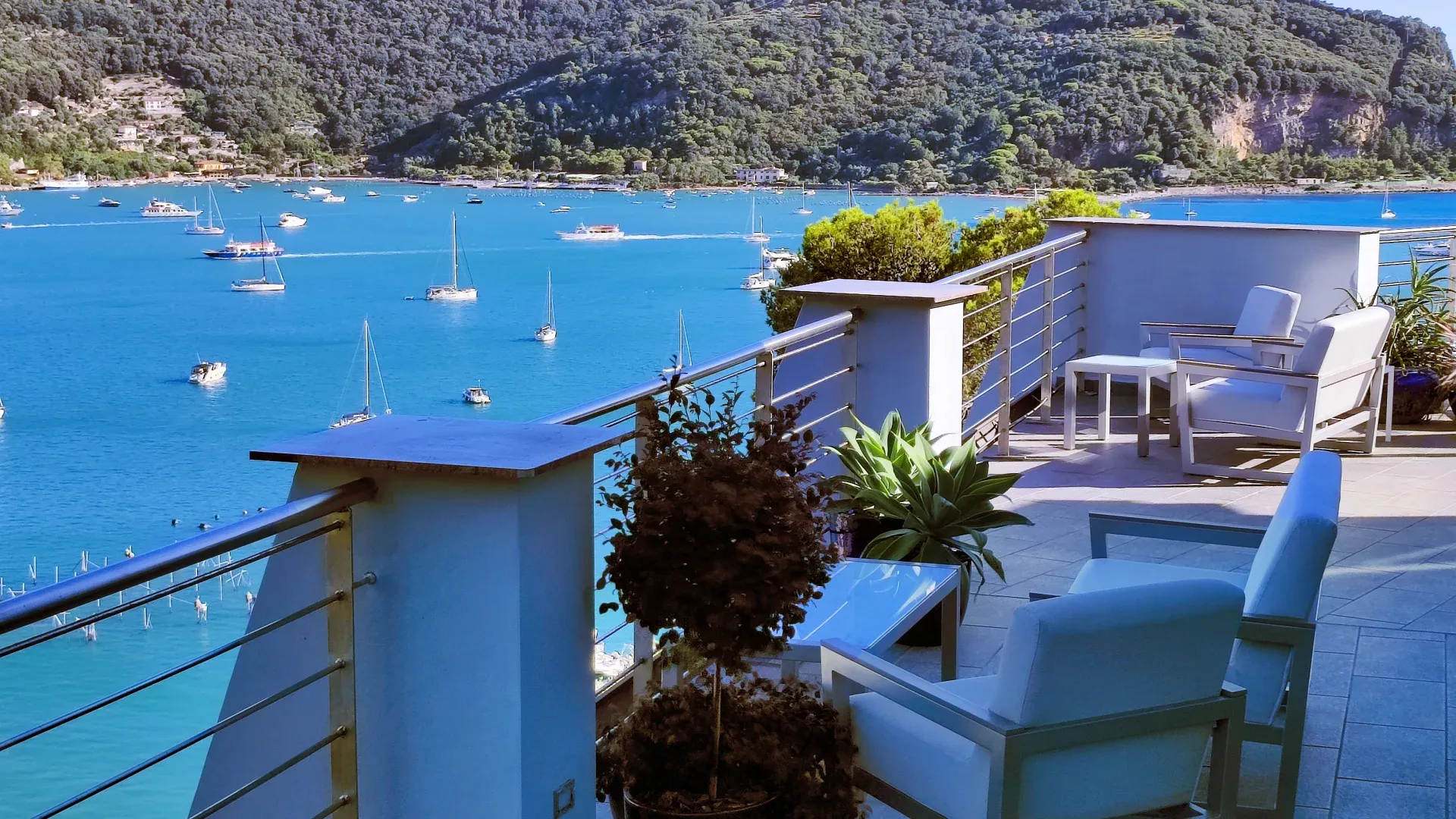 Terrazza con poltrone bianche affacciata sulla baia con barche a vela ormeggiate