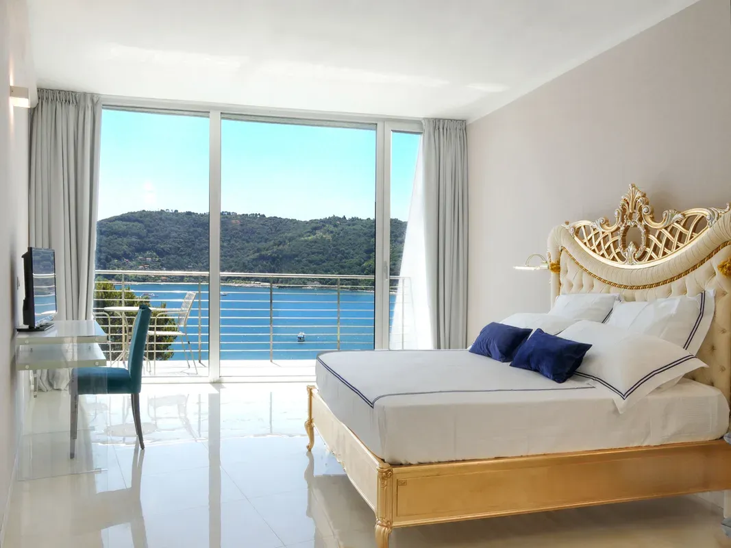 Camera elegante con letto matrimoniale dorato barocco e ampia vetrata vista mare