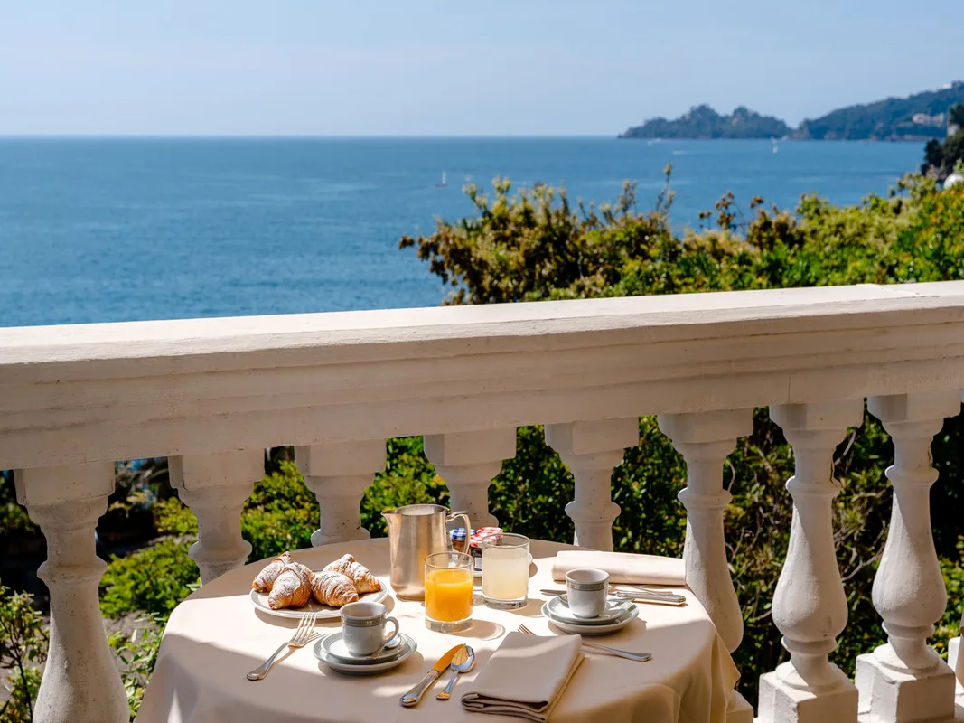 Colazione con cornetti e succo servita su balcone con balaustra e vista mare
