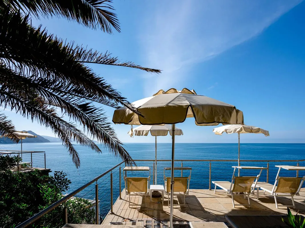 Terrazza solarium con lettini, ombrelloni e palma affacciata sul mare azzurro