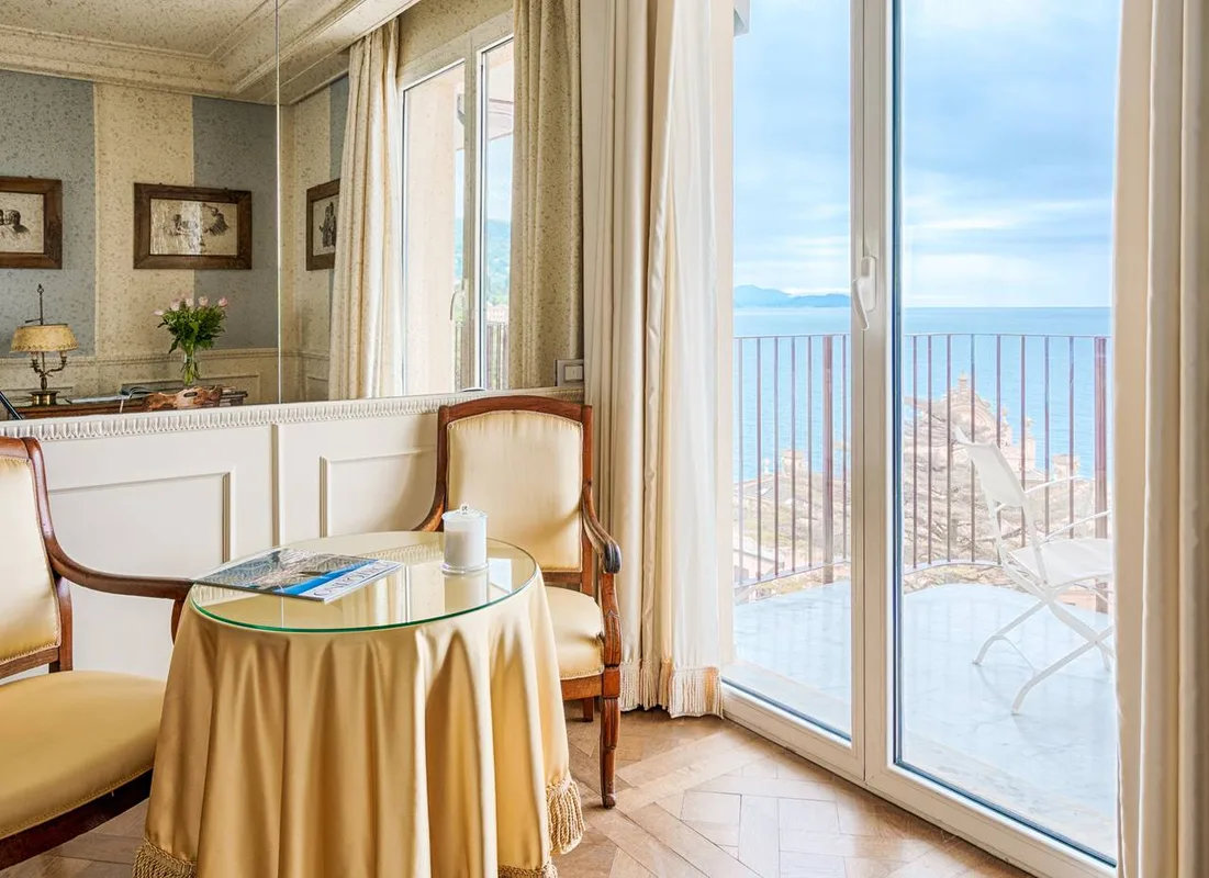 Angolo salotto con poltrone, tavolino e porta-finestra sul balcone vista mare