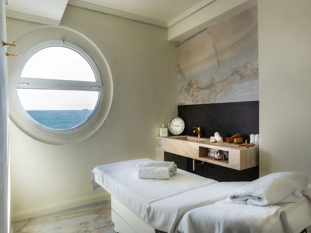 Cabina massaggi spa con lettino, oblò vista mare e lavabo in marmo