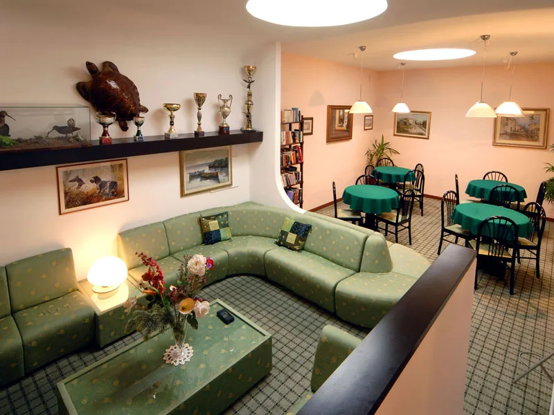 Sala lettura e relax con divano angolare verde, libreria e tavoli con sedie