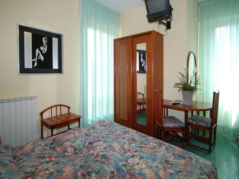 Camera con letto a fiori, armadio con specchio, scrivania e tende verdi
