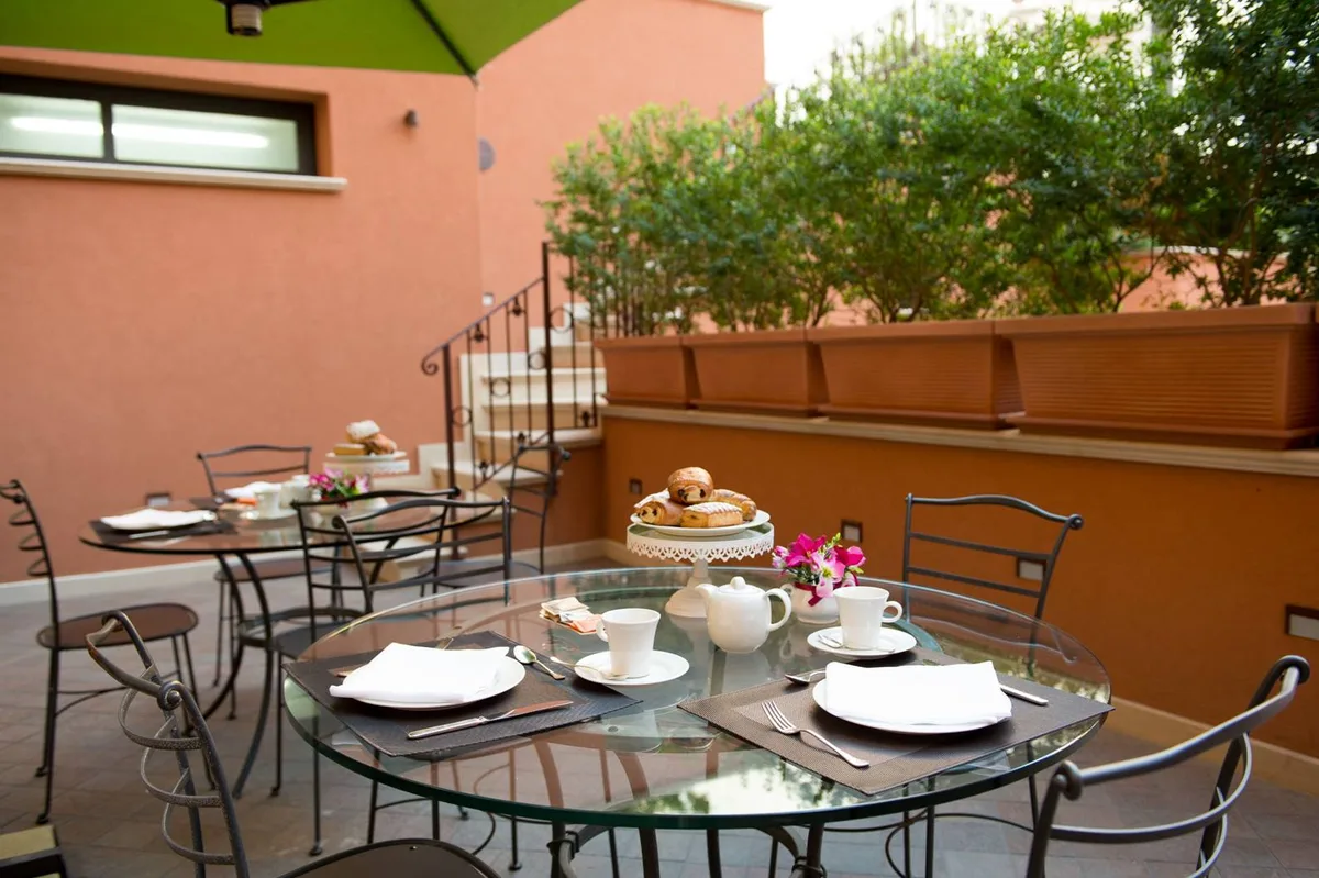 Terrazza per la colazione con tavolo in vetro apparecchiato, cornetti, tè e fiori