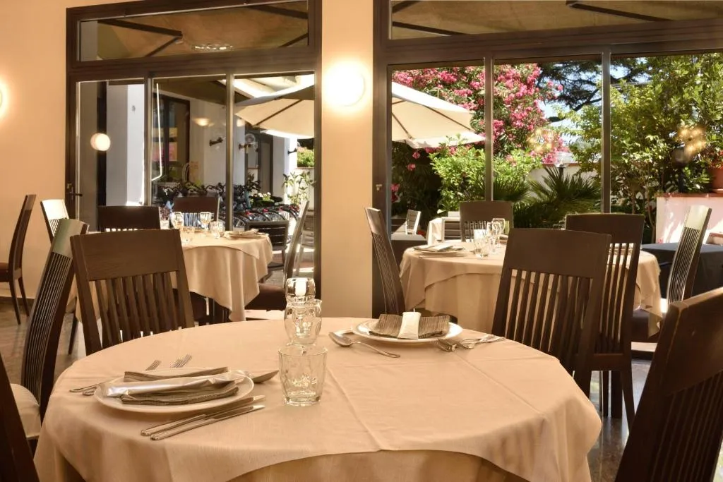 Sala ristorante con tavolo rotondo apparecchiato e vetrate sul giardino fiorito