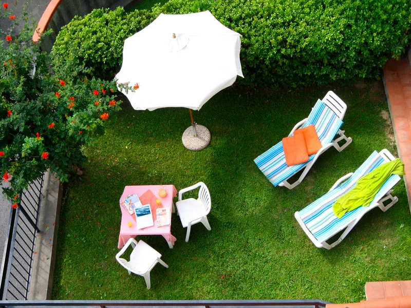 Vista dall'alto di giardino con ombrellone bianco, tavolino rosa e lettini prendisole