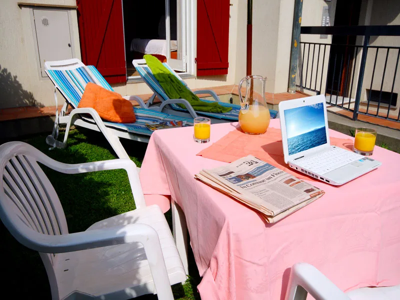 Tavolo da giardino con tovaglia rosa, succo d'arancia e laptop, lettini sullo sfondo