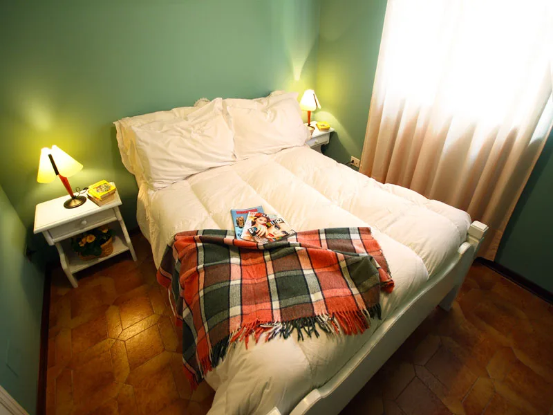Camera da letto matrimoniale con pareti verdi, lampade da comodino e plaid scozzese