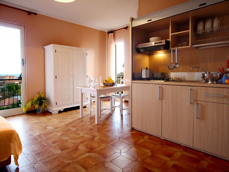 Cucina con angolo cottura attrezzato, armadio bianco, tavolo e accesso al balcone con vista