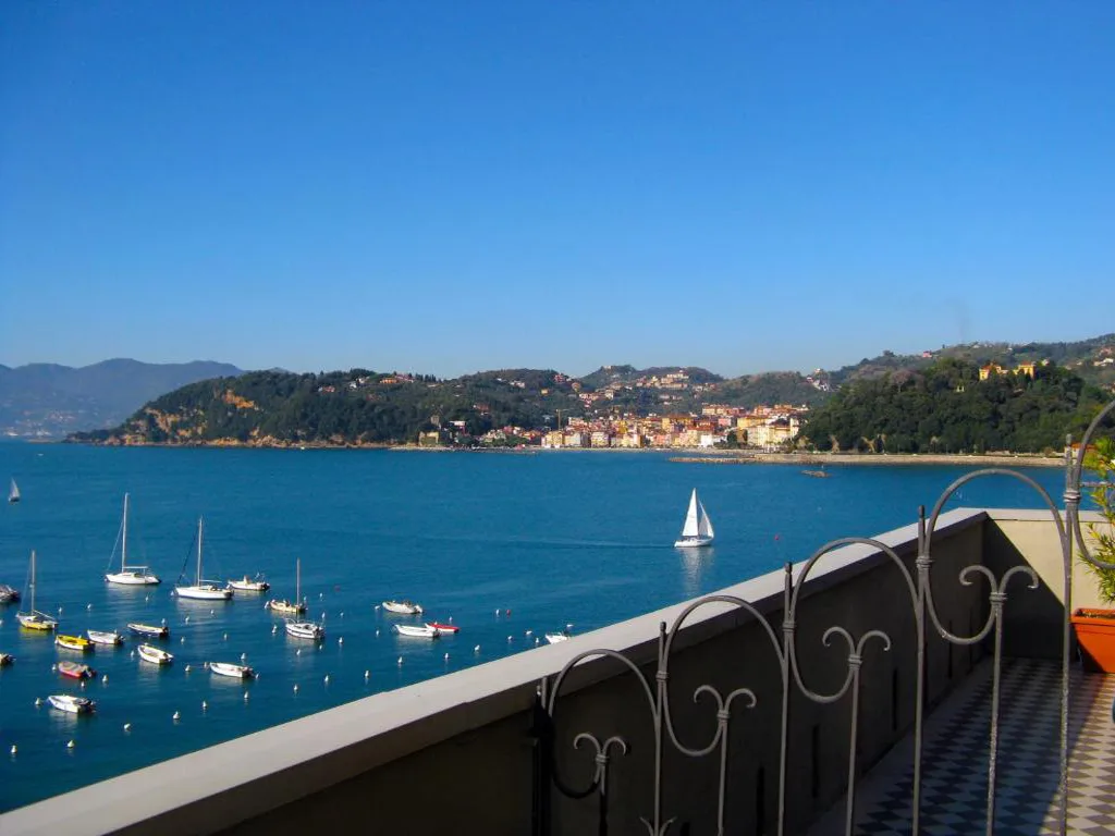 Vista panoramica dal balcone sul golfo con barche a vela e colline al tramonto