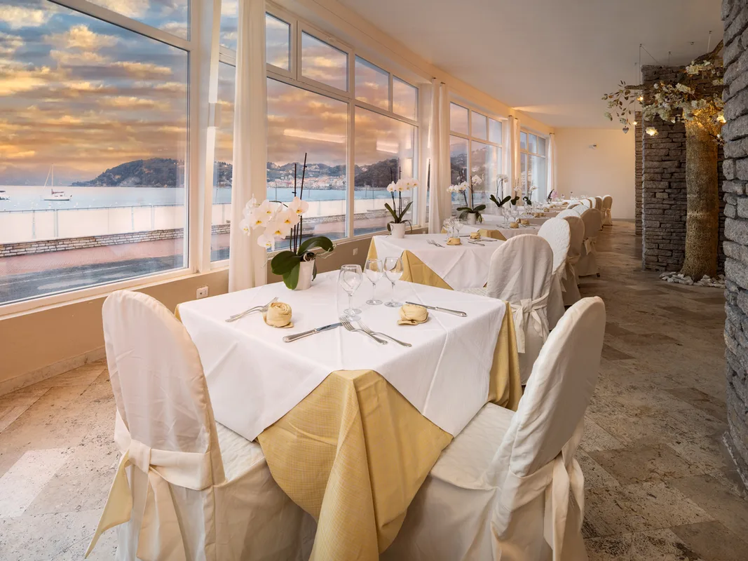 Sala ristorante elegante con tavoli apparecchiati e vetrate sul mare al tramonto