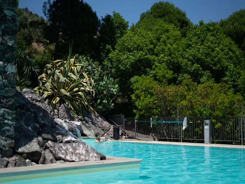 Piscina all'aperto con acqua turchese circondata da rocce e vegetazione mediterranea