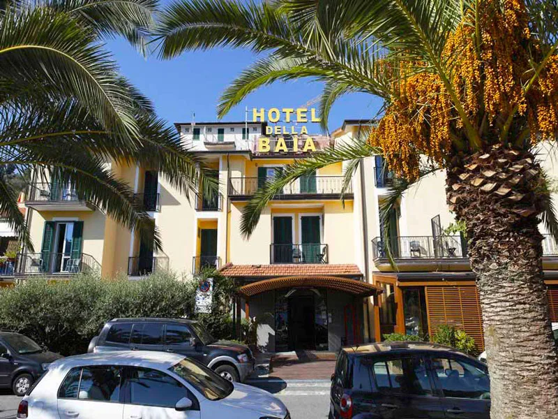 Facciata gialla dell'Hotel della Baia con palme e parcheggio antistante