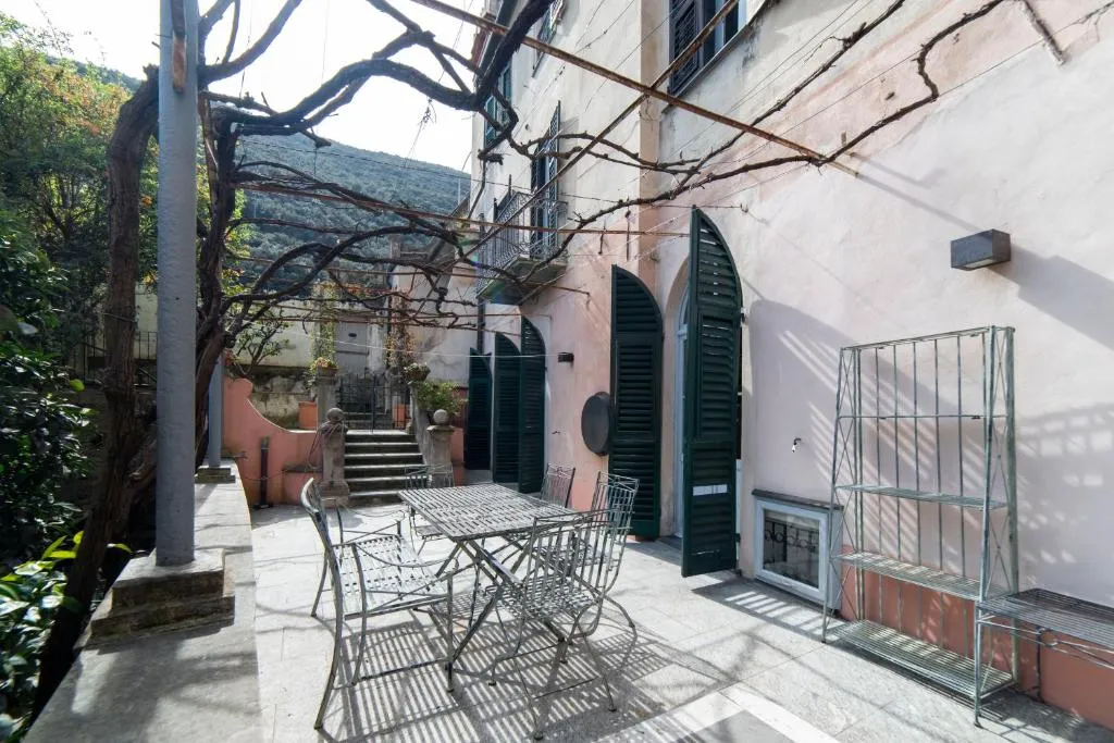 Terrazza esterna con pergolato, tavolo e sedie in ferro tra edifici e colline