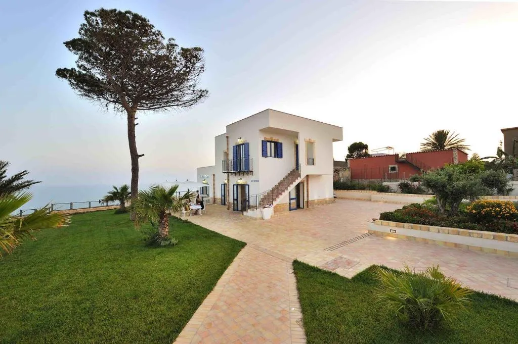 Edificio bianco con persiane blu e scalinata esterna, circondato da giardino e pino vista mare