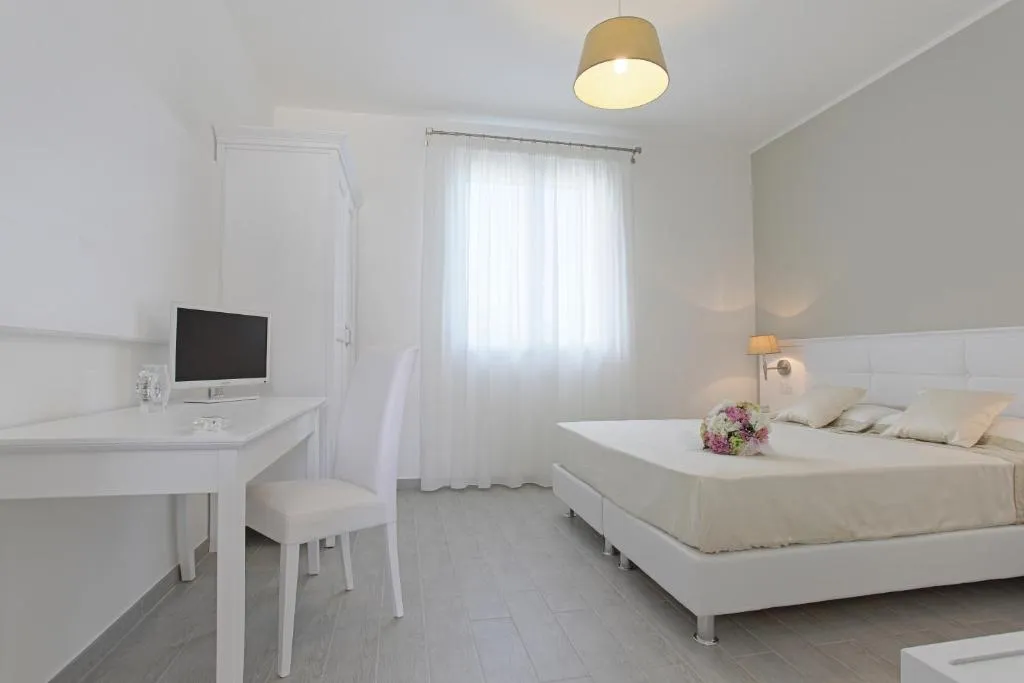 Camera bianca con letto matrimoniale, scrivania con TV e finestra con tende