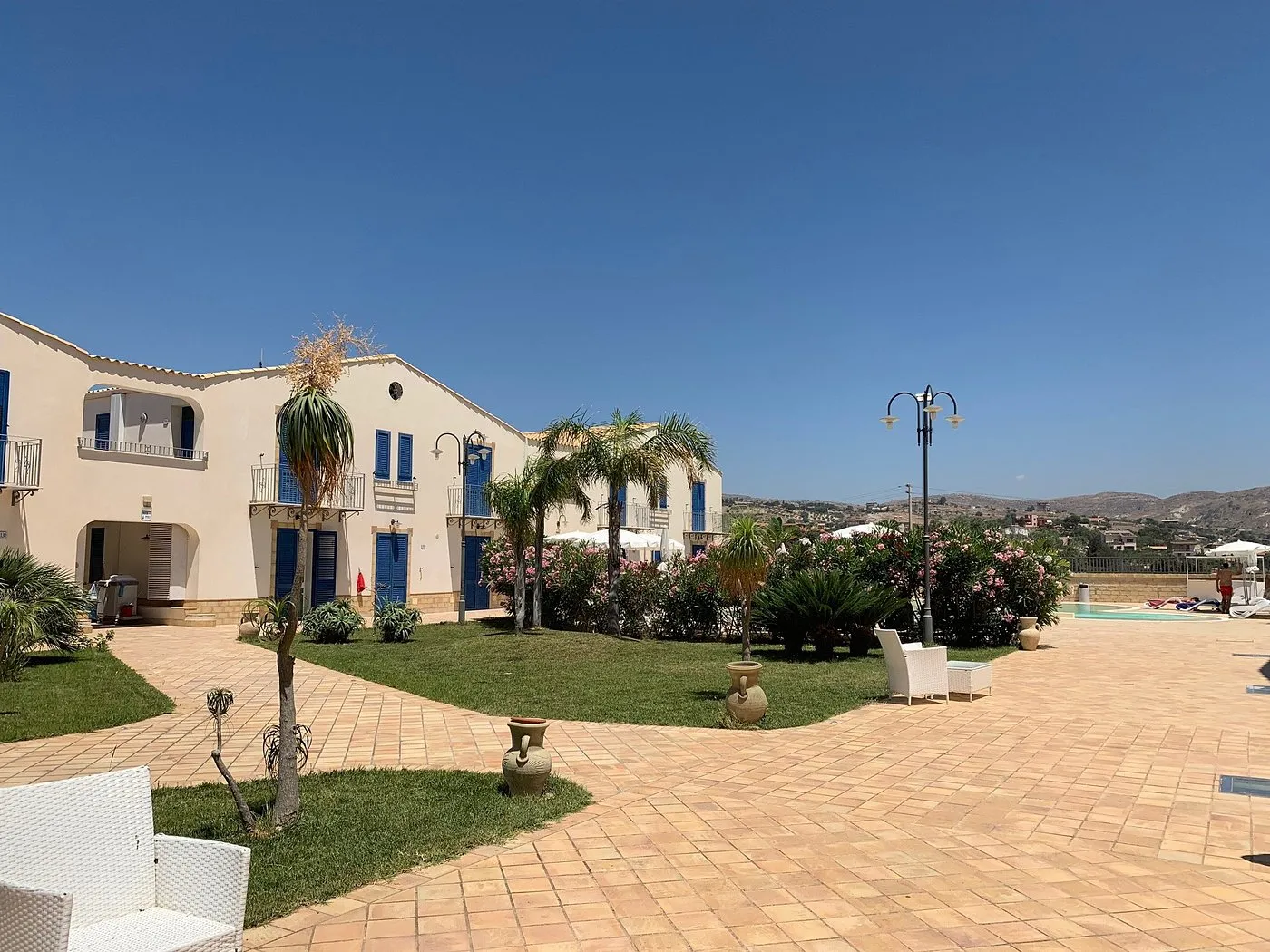 Cortile del residence con giardino curato, palme, fiori e pavimentazione in cotto vicino alla piscina