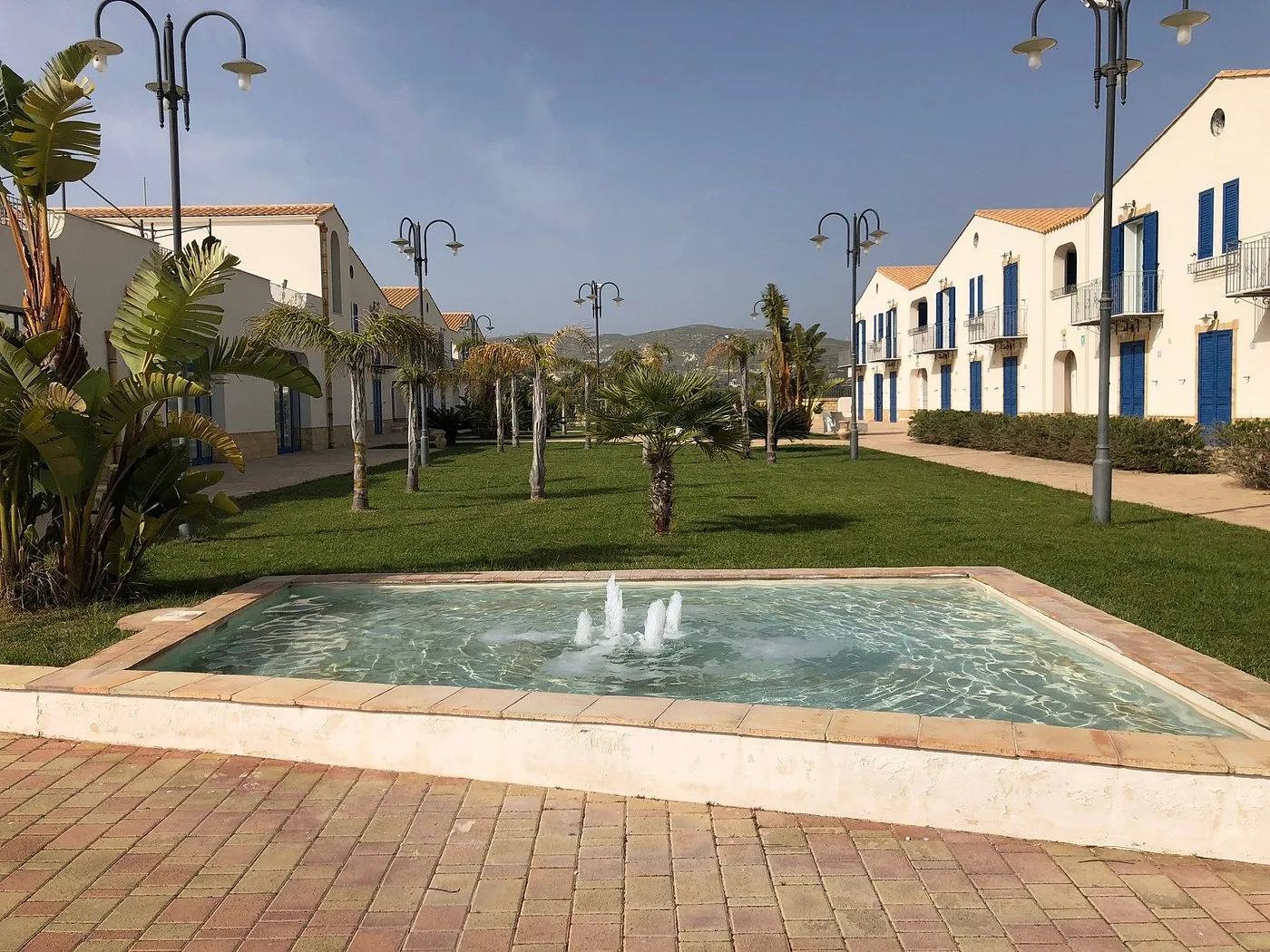Fontana con getti d'acqua nel giardino del residence con palme ed edifici con persiane blu