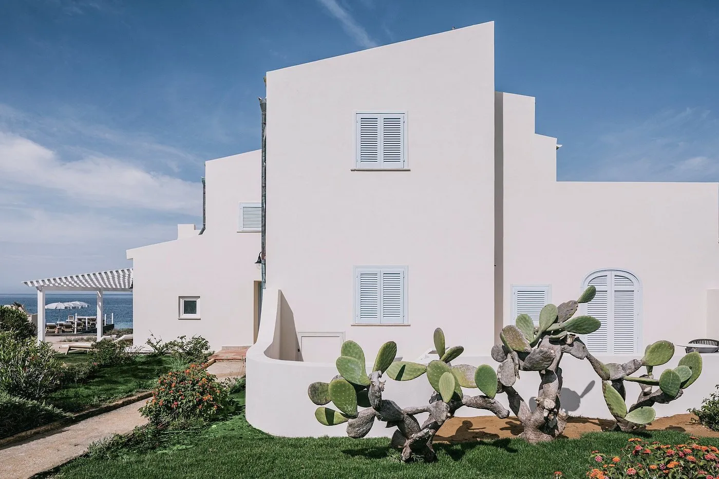 Esterno di edificio bianco con persiane azzurre, prato e cactus vista mare
