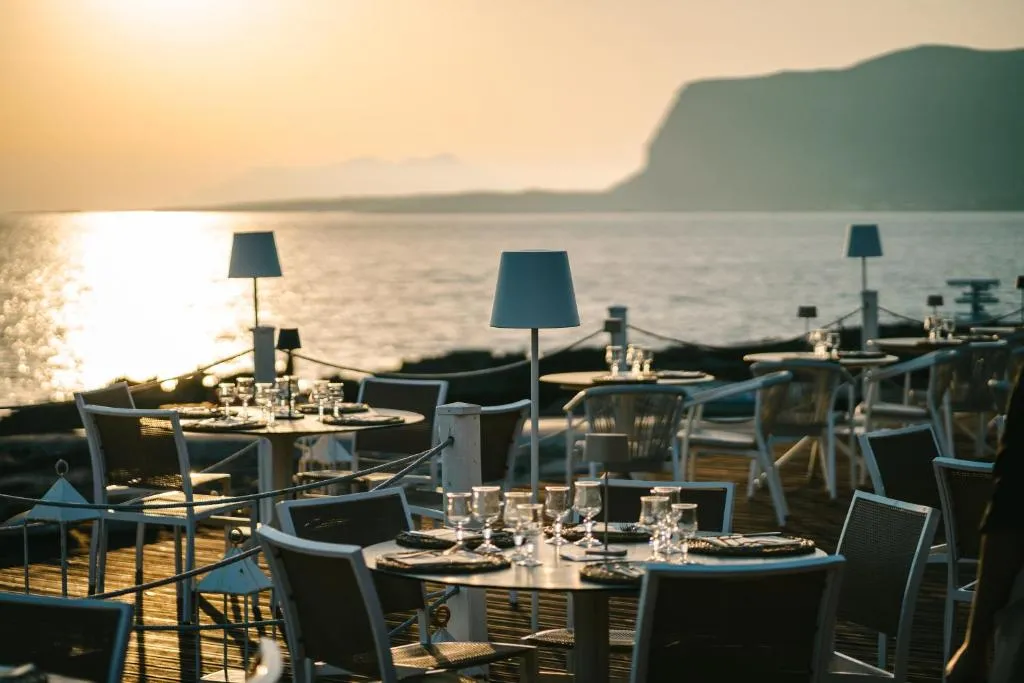 Ristorante all'aperto con tavoli apparecchiati e lampade vista mare al tramonto
