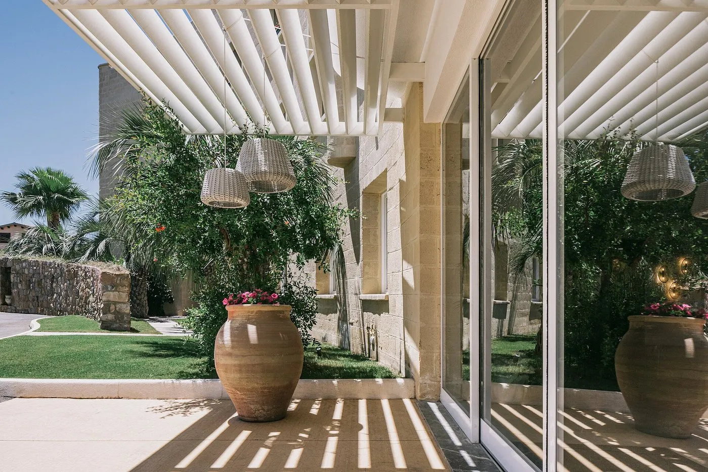 Patio esterno con pergolato bianco, vaso in terracotta e lampade in vimini