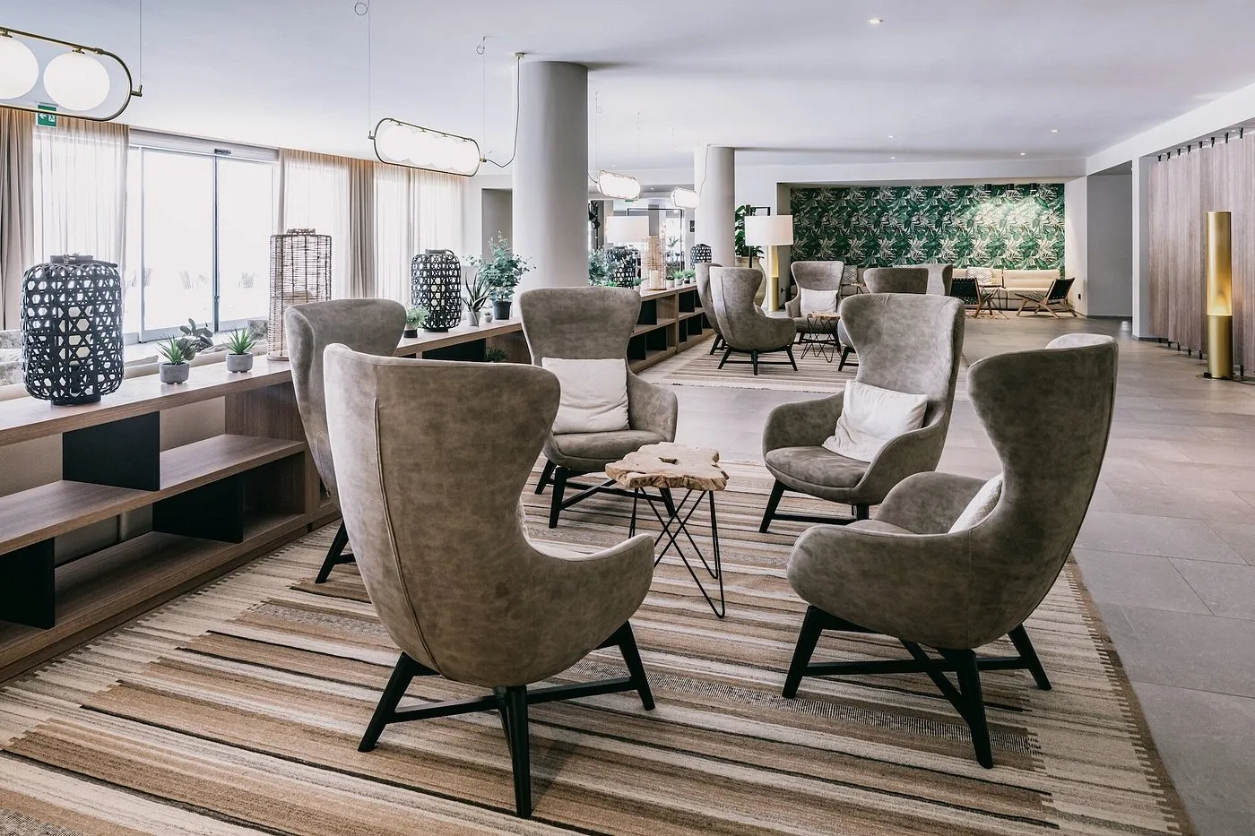 Hall dell'hotel con poltrone grigie, tavolini in legno e parete decorata con motivi tropicali