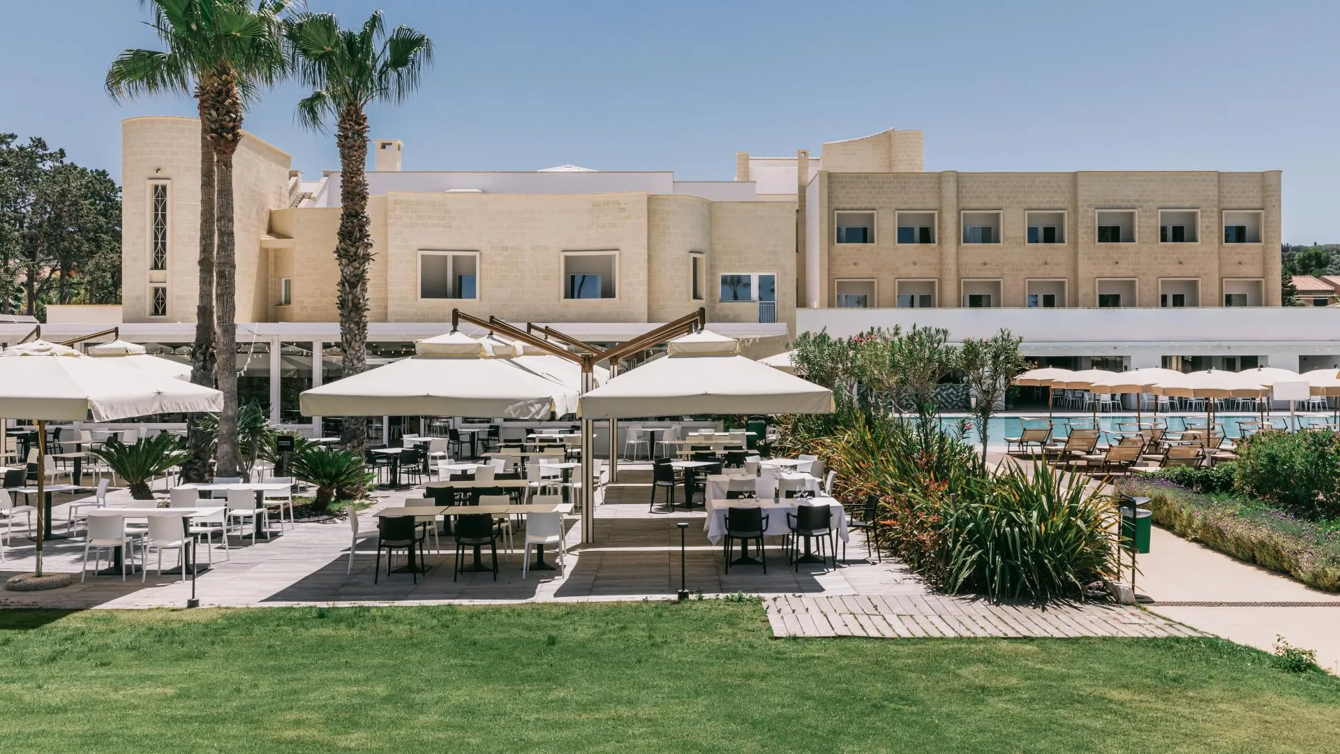Ristorante esterno con tavoli, sedie e ombrelloni bianchi accanto alla piscina