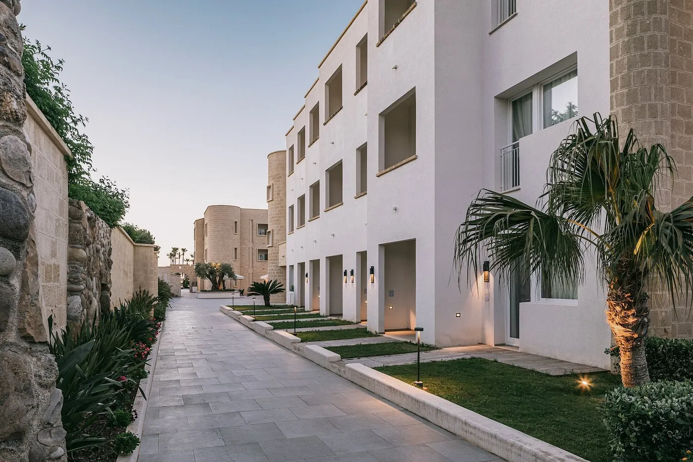 Vialetto pedonale tra gli edifici dell'hotel con giardini e palme al crepuscolo