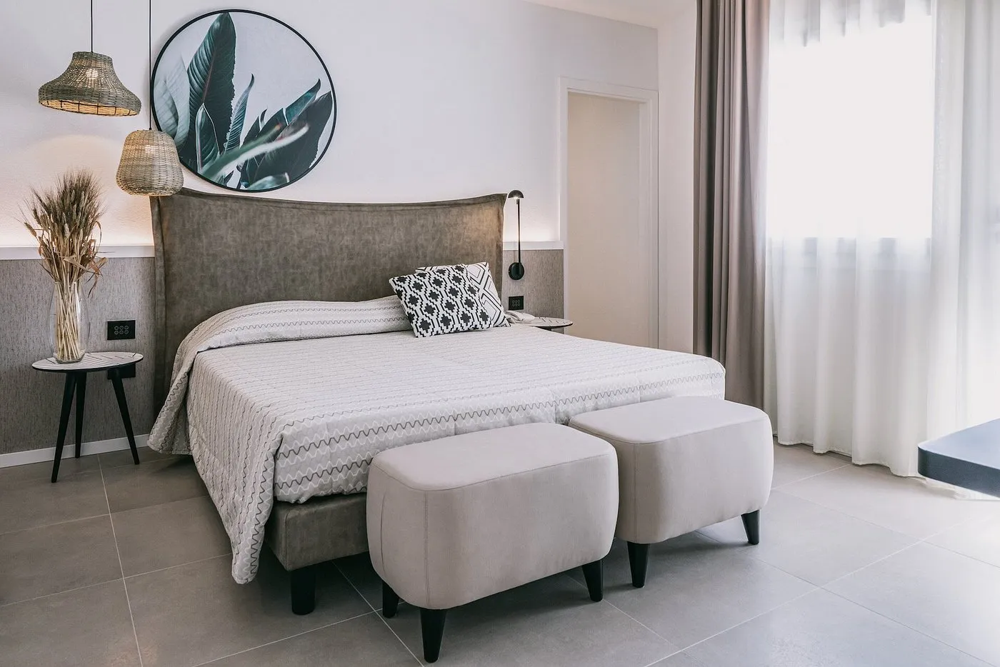 Camera matrimoniale con testiera imbottita, pouf e decorazione tropicale alla parete