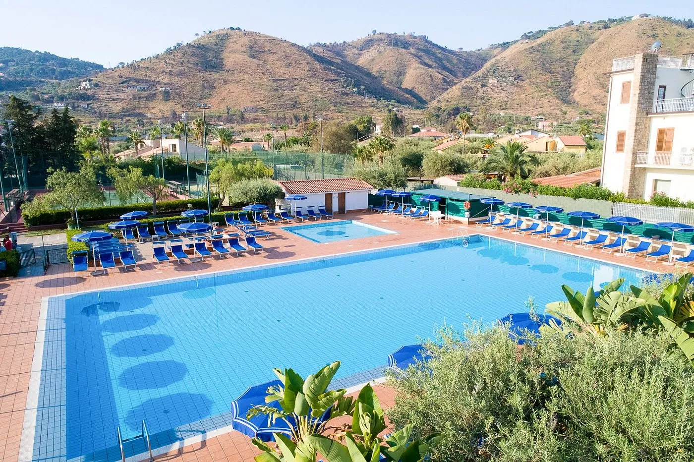 Grande piscina con lettini e ombrelloni blu circondata da colline