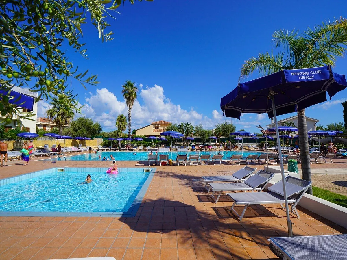 Piscina del resort con ombrelloni blu, palme e cielo azzurro